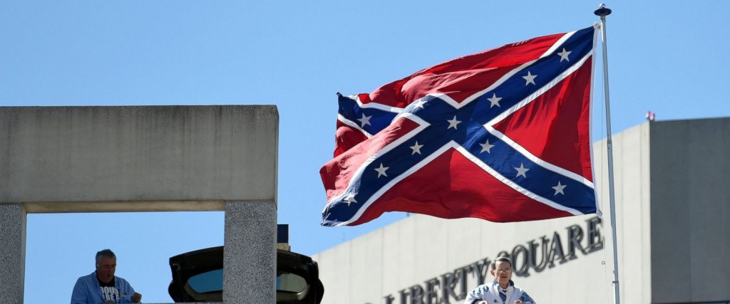 Basketball fans look out as a Confederate flag flies from a parking deck outside the arena before a second-round game of the NCAA men's college basketball tournament in Greenville, S.C., Sunday, March 19, 2017. A small group of protesters flew a large Confederate flag from the top of a parking garage next to the arena hosting two men's NCAA Tournament games. (AP Photo/Rainier Ehrhardt)