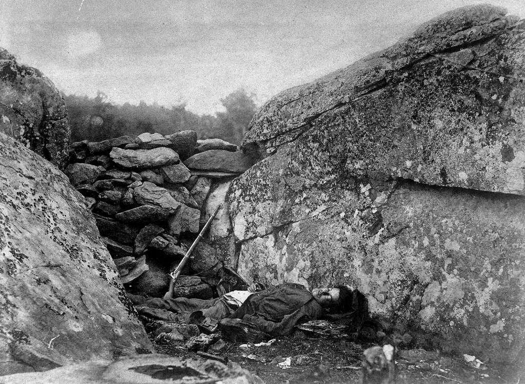 Slain rebel sharpshooter slumped down in his ineffective hideout, w. his rifle still perched against rocks, at end of Battle of Gettysburg during the Civil War.